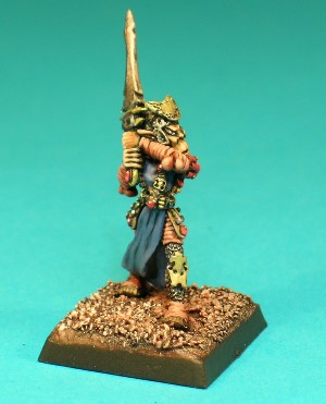 Pose 3, variant A. This Githyanki warrior wields a straight-bladed two-handed sword with an ornate hilt. He wears chainmail leggings with metal greaves, and armour patterned with beads, leather strips and jewels. He wears a flowing surcoat, and his leather strips bound around his arms. This particular variant wears a pitted, conical helmet with small cheekguards which allow his large, pointed ears to protrude, and a crescent shaped plate on the front. He is looking straight forwards with his mouth closed in a look of grim determination.
